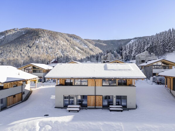 A modern ski resort with wooden cabins and a central building with large windows and a covered patio area.