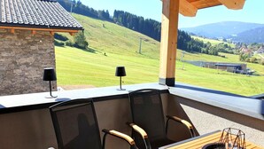 Une terrasse avec une table et des chaises, un mur en pierre et une vue sur un paysage verdoyant avec des collines.