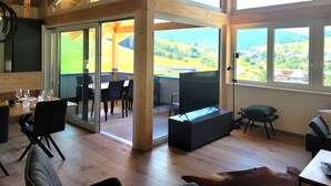 A spacious room with a high ceiling, wooden beams, large windows, and a view of a green landscape. - Lovely ski in-ski out lodge with sauna (Sankt Lambrecht)