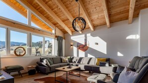 A modern living room with a wooden ceiling, large windows, a sectional sofa, a leather chair, and a cowhide rug. - Lovely ski in-ski out lodge with sauna (Sankt Lambrecht)