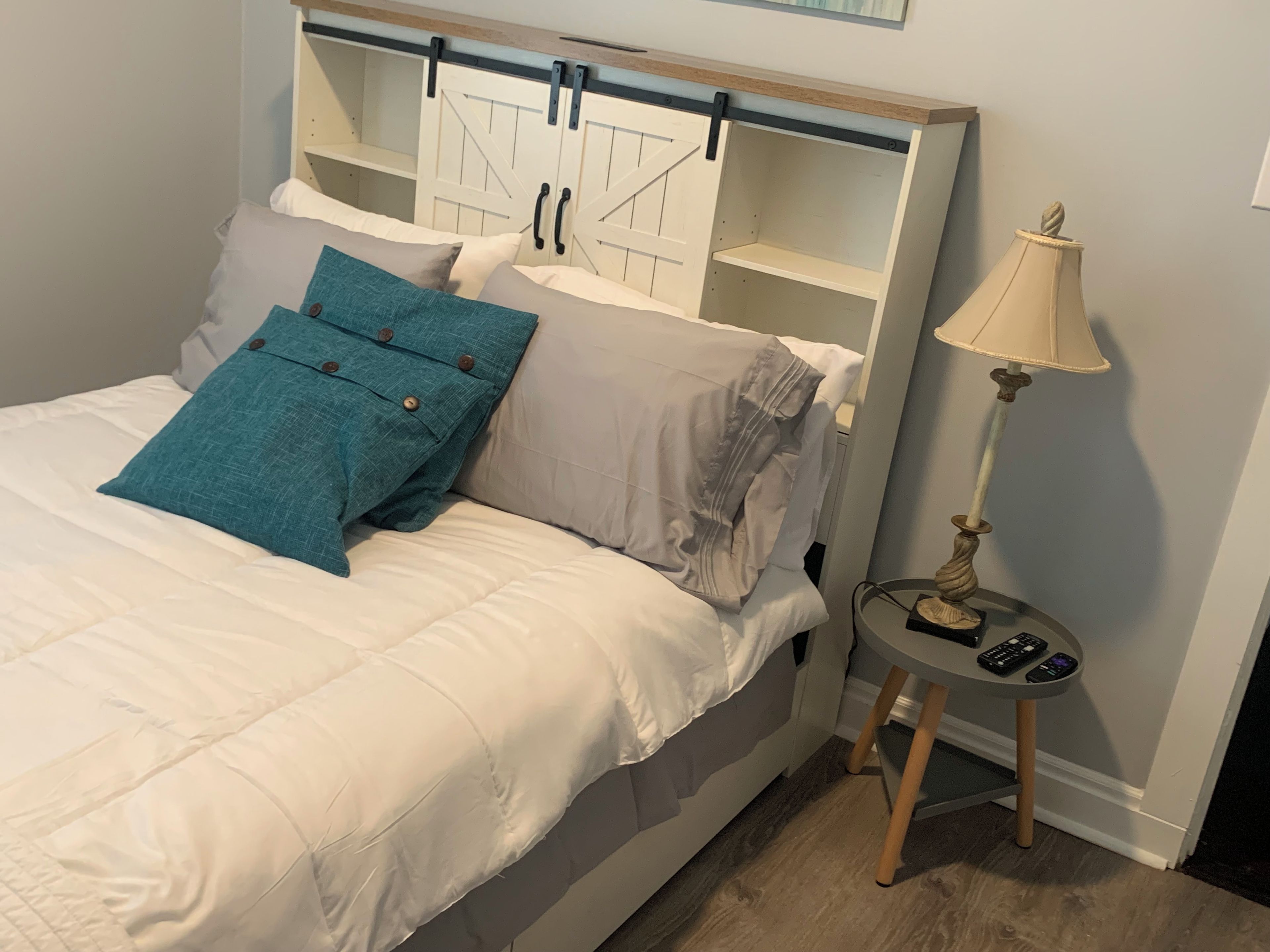 Ein Bett mit Kopfteil, Kissen, einem Nachttisch mit Lampe und einer Fernbedienung.