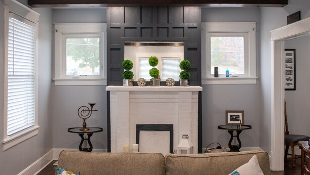 A living room with a fireplace, two windows, a sofa, and a small table. - Cozy Cottage within walking distance of downtown! (Bristol)