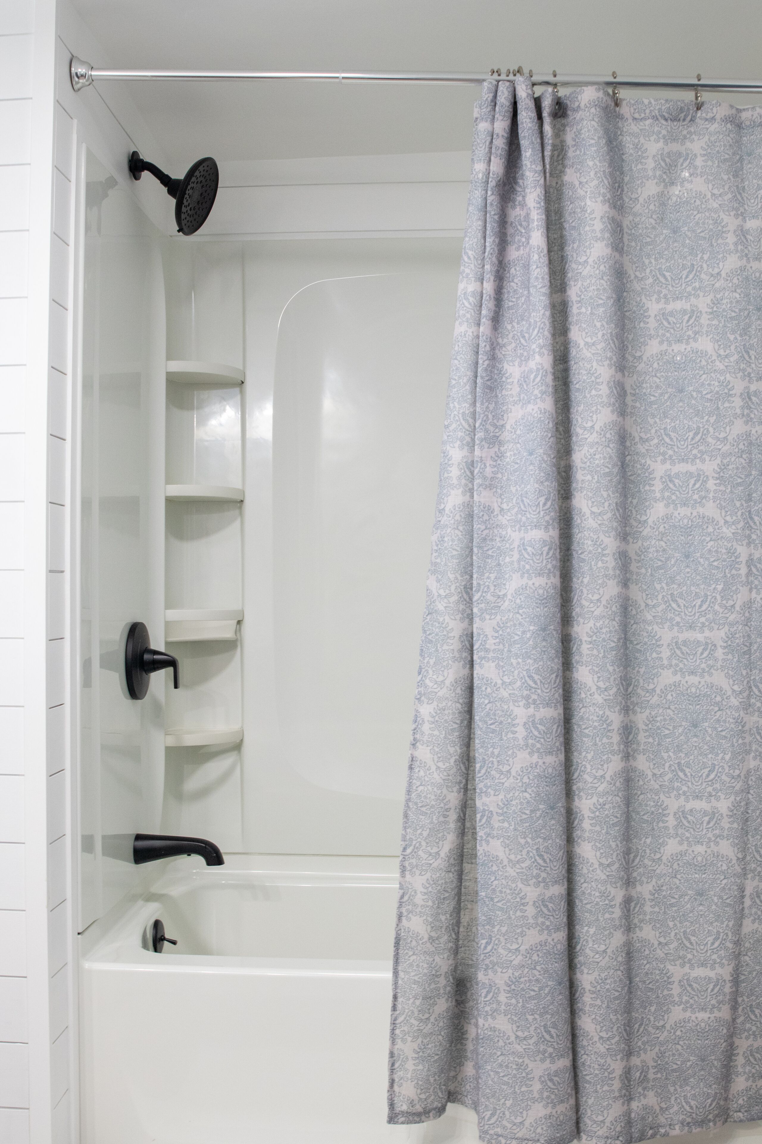 A modern bathroom with a white bathtub, a shower with a black handheld showerhead, and a grey patterned shower curtain.