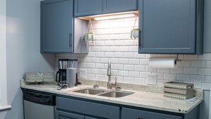 A kitchen with blue cabinets, a dishwasher, a coffee maker, and hanging plants. - Cozy Cottage within walking distance of downtown! (Bristol)