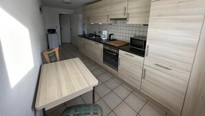 Et lille køkken med lyse træskabe, en sort bordplade og et flisebeklædt bagpanel.