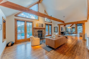 A spacious living room with a fireplace, wooden beams, large windows, and a view of the outdoors. - The Sunflower-Secluded luxury,hot tub,minutes to town (Skyland & Surrounding Areas)