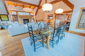 A spacious living area with a large sofa, a glass dining table with chairs, and a stone fireplace.