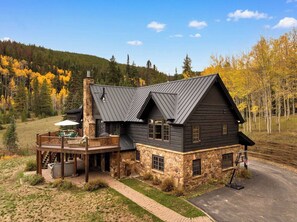 Une cabane en rondins à deux étages, avec des fondations en pierre, un balcon doté de mobilier d’extérieur et un panier de basketball.