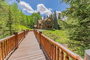 A wooden bridge leading to a lodge surrounded by forest.