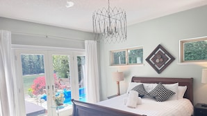 A bedroom with a large bed, two bedside lamps, a chandelier, and a view of a garden through a sliding glass door. - ocean dock and pool art villa  (Ladysmith)