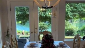 A dining area with a table set for six, a chandelier, and large windows with a view of greenery. - ocean dock and pool art villa  (Ladysmith)