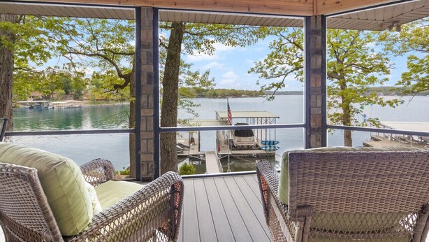Eine überdachte Terrasse mit Korbmöbeln und Blick auf einen See und eine Anlegestelle.