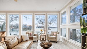 Ein geräumiges Wohnzimmer mit großem Fenster mit Seeblick, einem Ledersofa, zwei Sesseln und einem Couchtisch mit dekorativen Accessoires.