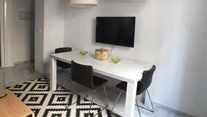 A dining area with a white table, black chairs, and a flat-screen TV mounted on the wall.