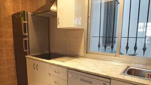 A compact kitchen with a built-in dishwasher, a stove, and a window with a metal grill.