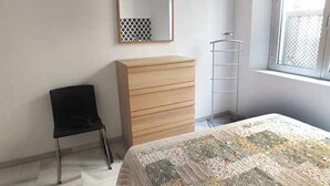A bedroom with a bed, a dresser, a chair, a window, and a mirror.