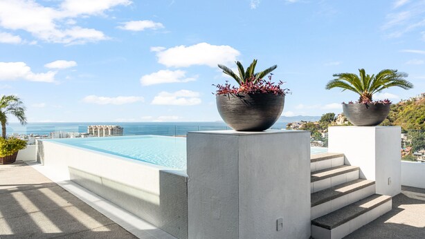Ein Poolbereich auf dem Dach mit freiem Blick auf den Ozean, ein großer Pflanzkübel mit Pflanzen und ein Satz aus Betontreppen, die zum Pool führen.