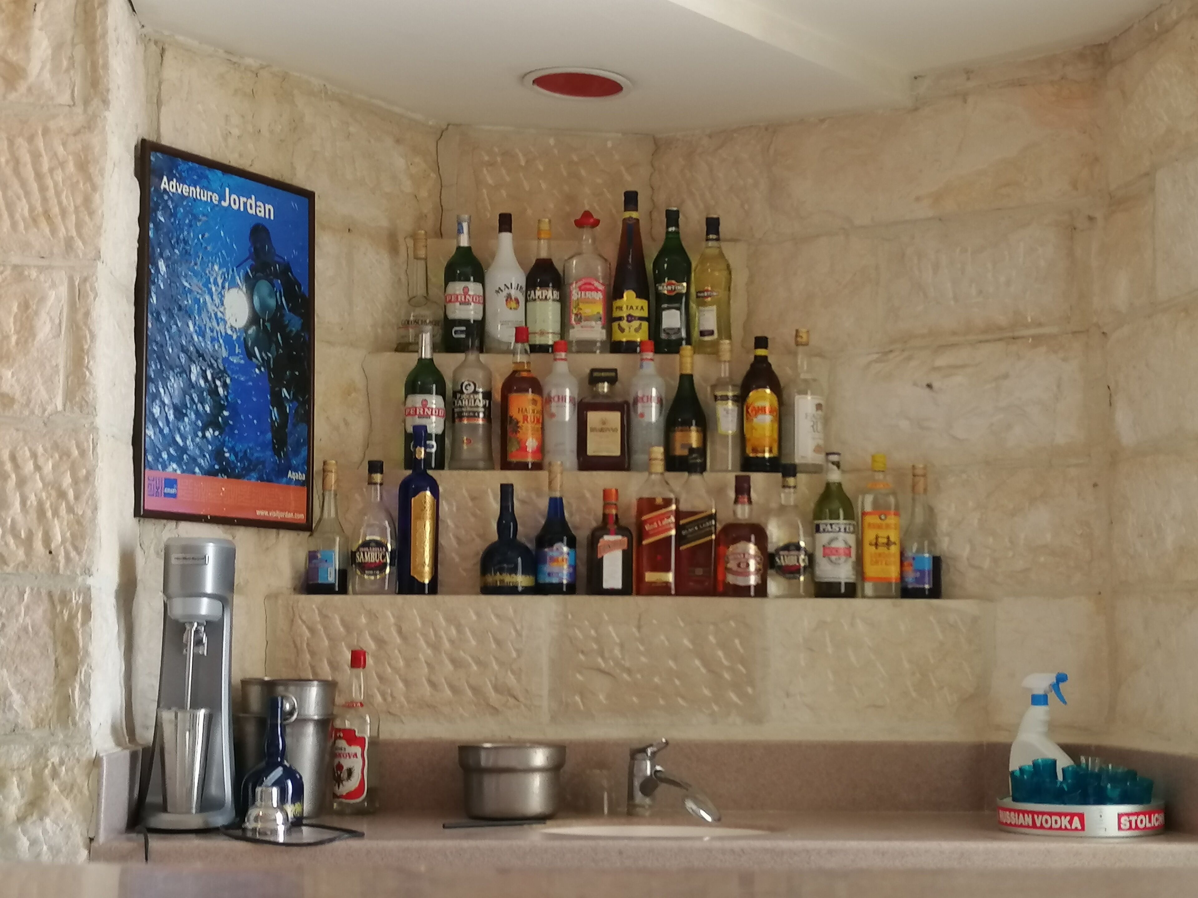 Uma área de bar com diversas garrafas de bebidas e um cartaz na parede.