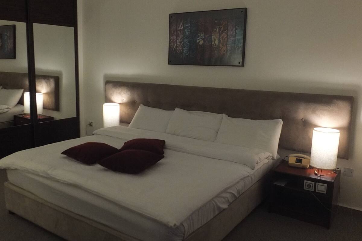 A hotel room with a large bed, two bedside lamps, a nightstand with a telephone, and a painting on the wall.
