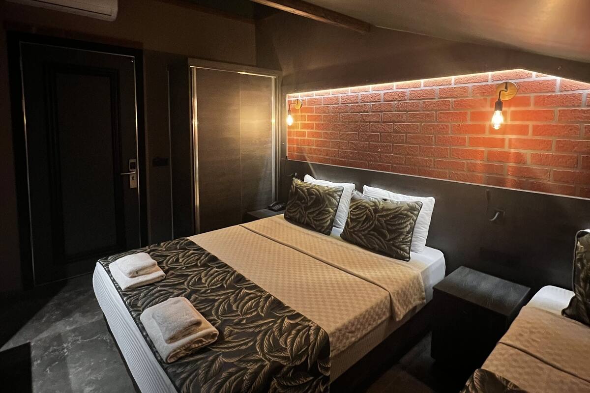 Una habitación de hotel moderna con una cama grande, una mesita de noche pequeña y una pared de ladrillo decorativa.