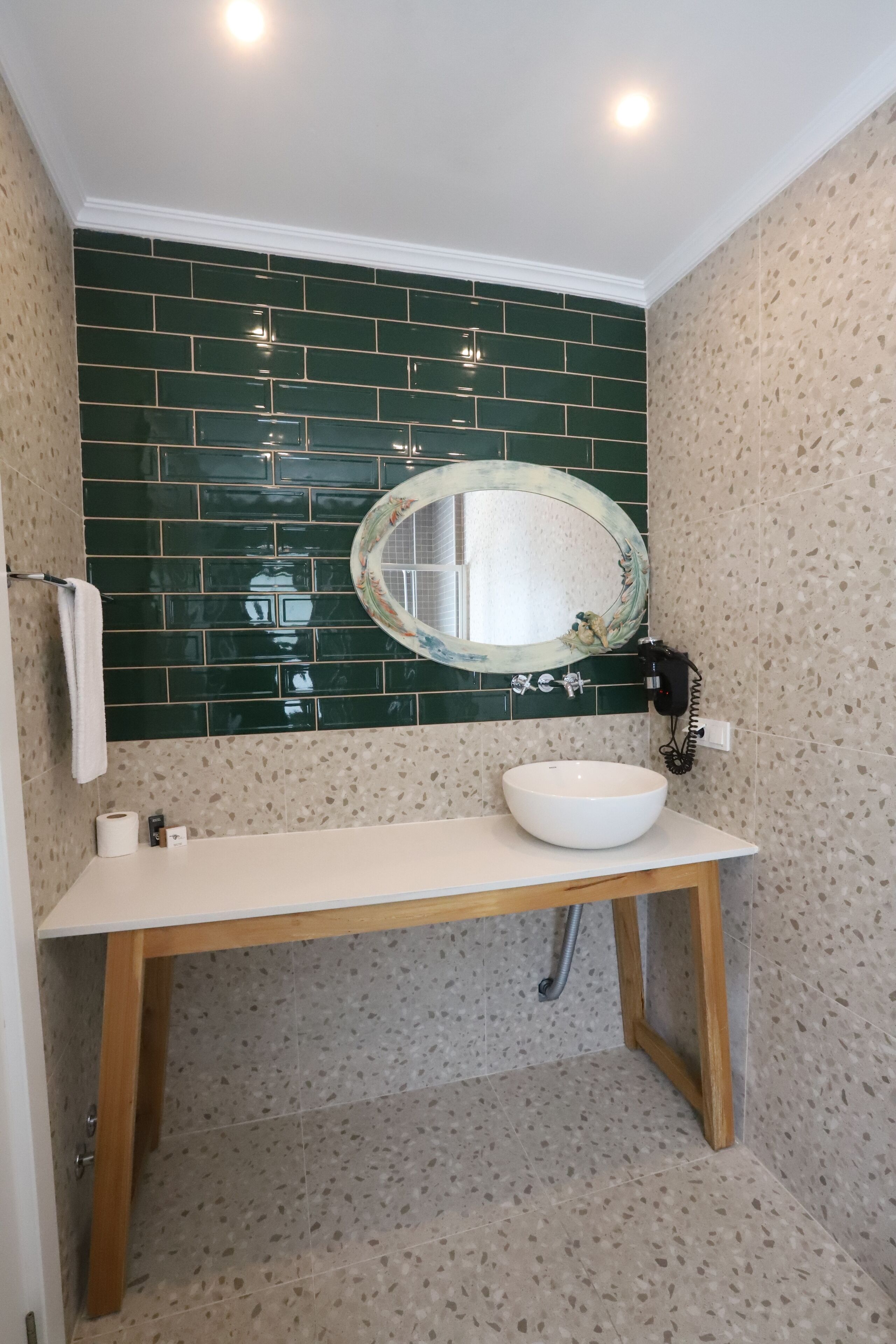 A bathroom with a white sink, green tiled backsplash, and a round mirror.