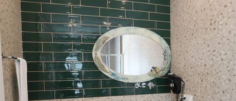 A bathroom with a white sink, green tiled backsplash, and a round mirror.