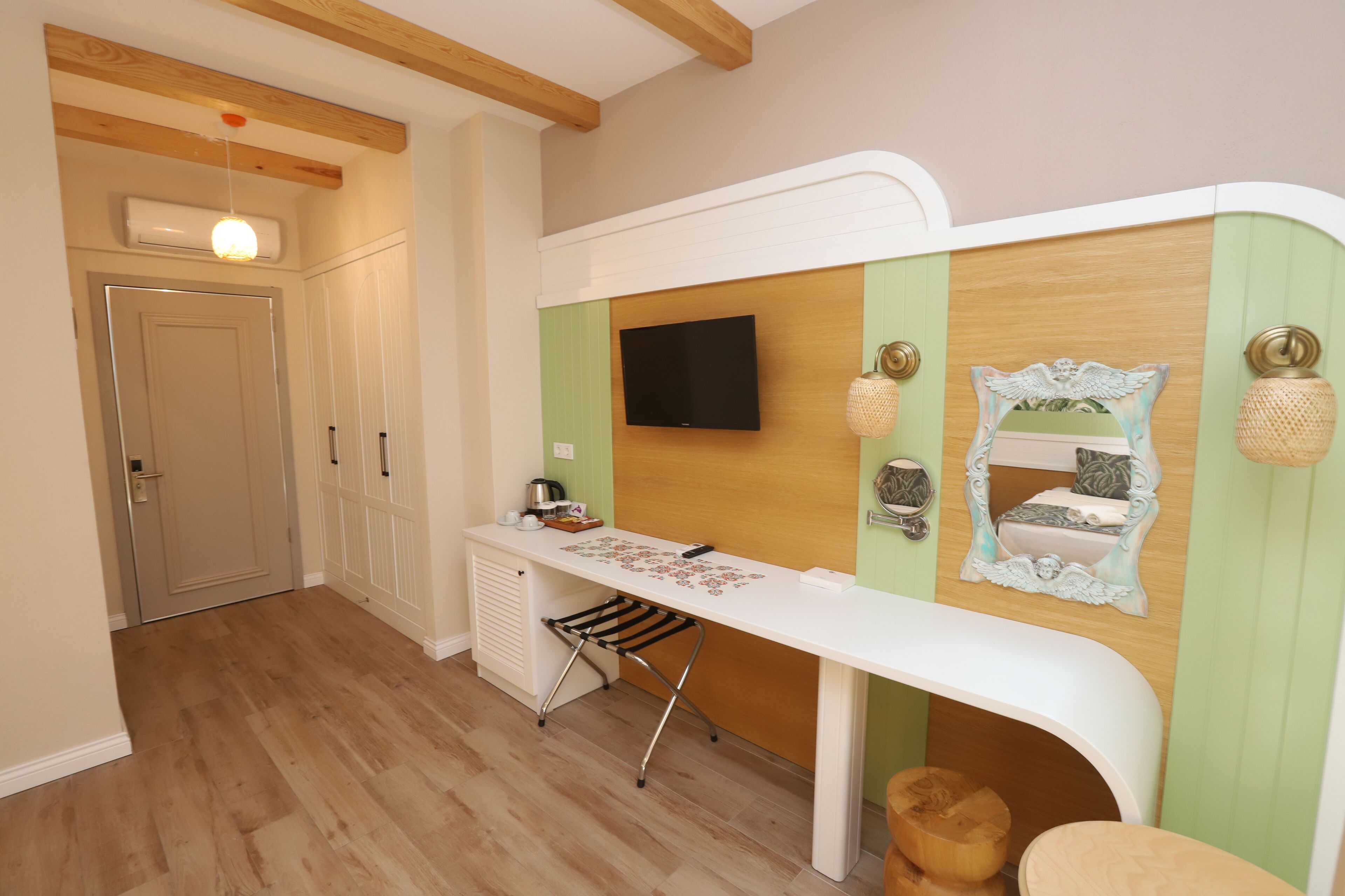 A room with a wooden floor, a white desk with a flat-screen TV, a small chair, and a decorative mirror.