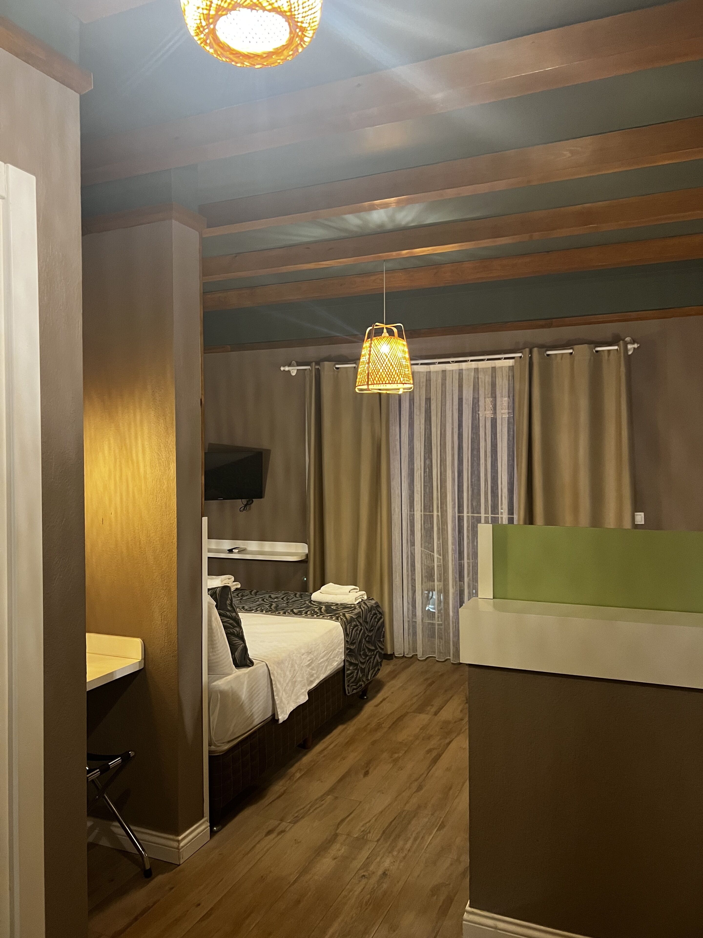 A compact hotel room with a bed, a small desk, a mirror, and a television.