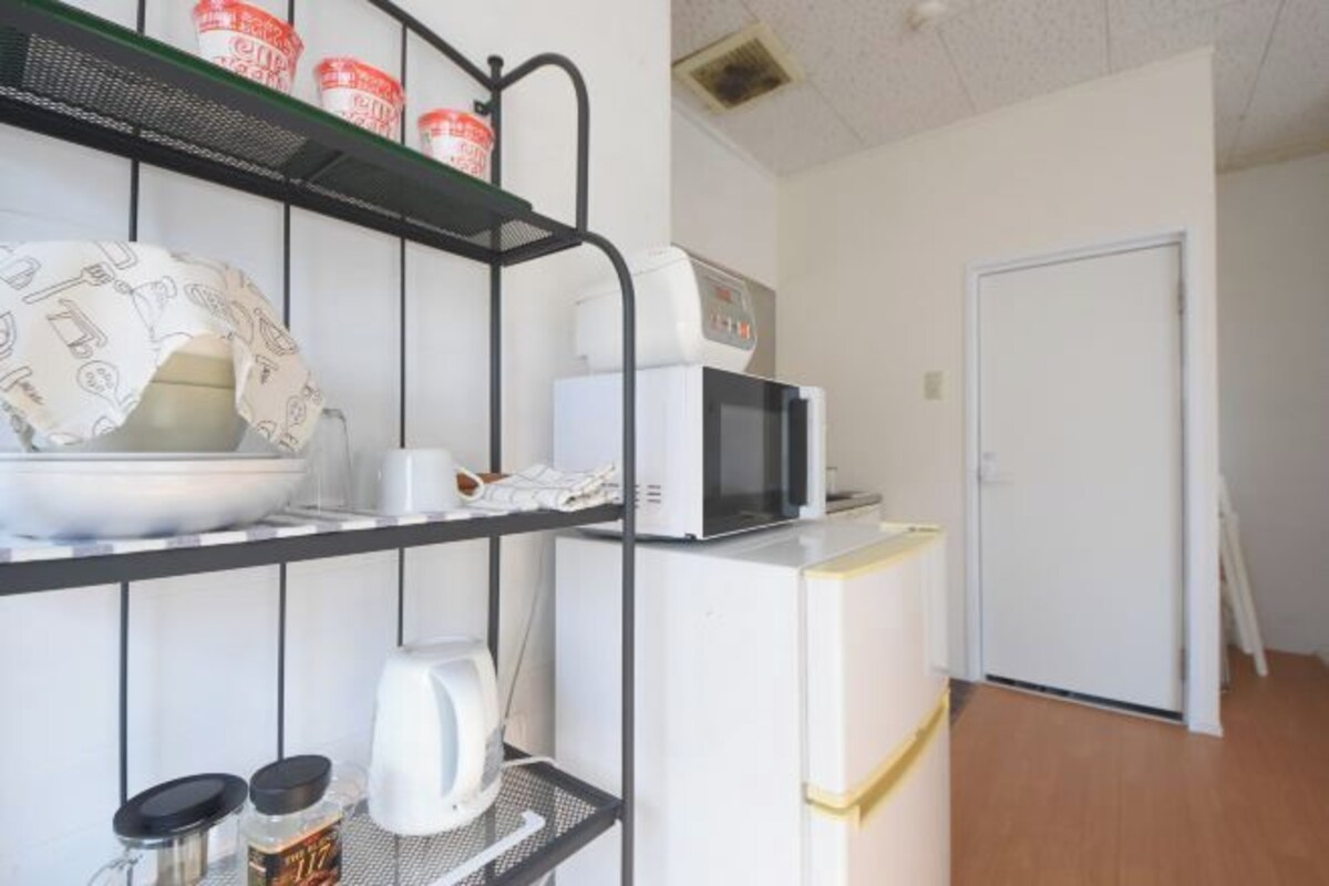 A kitchenette with a microwave, kettle, and shelves with kitchenware.