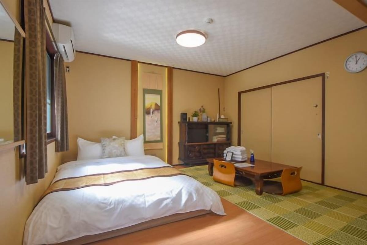 A hotel room with a bed, a desk, a wardrobe, and a clock on the wall.