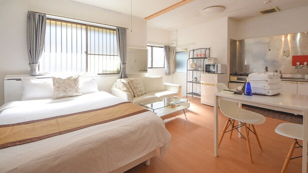 A hotel room with a large bed, a sitting area with a sofa and armchairs, a small kitchen area, and a dining table with chairs. - Comfy Stay MR2 (Nara)