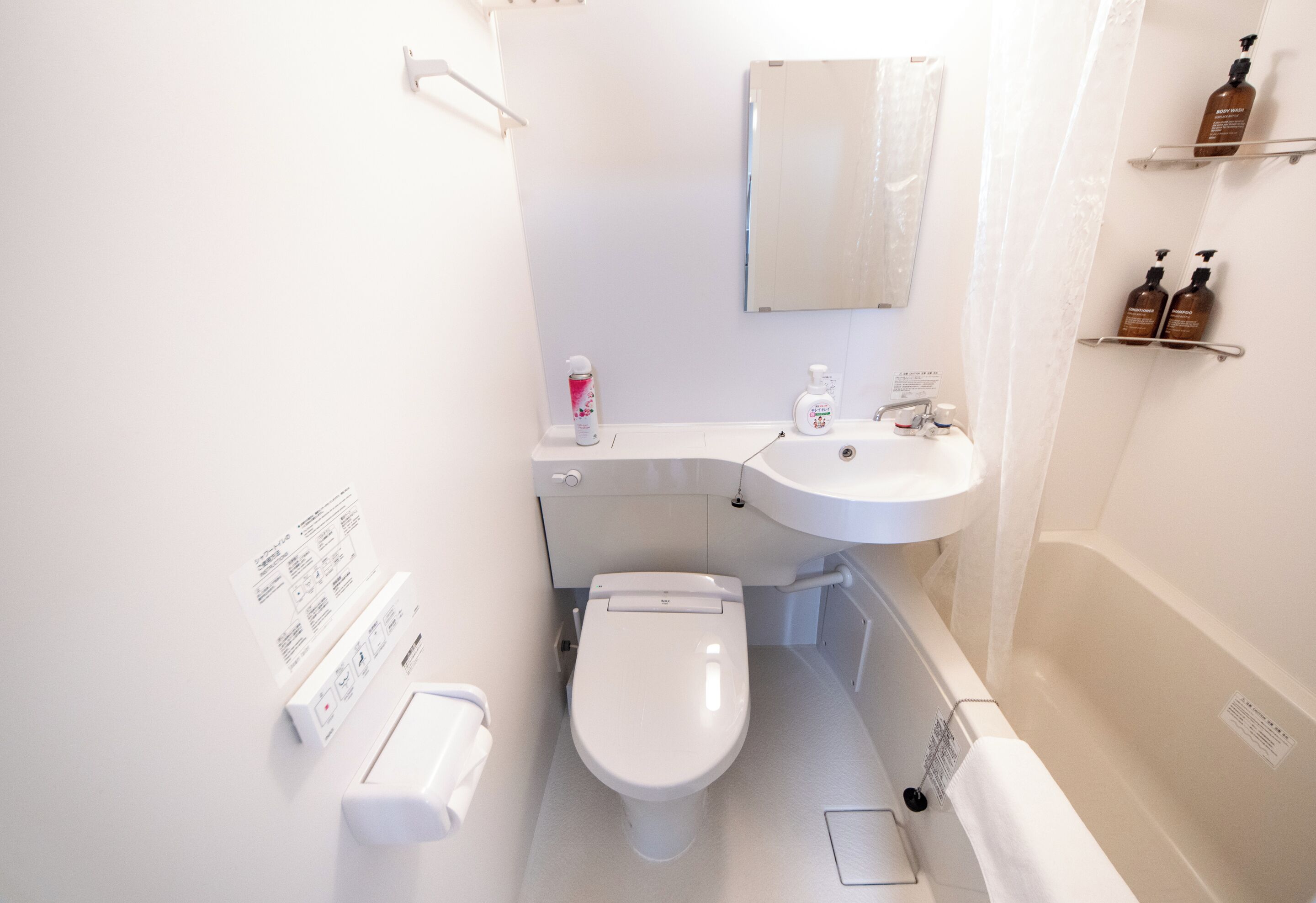 Uma casa de banho compacta com sanita, lavatório e banheira. Há produtos de higiene pessoal na parede e um dispensador de papel.