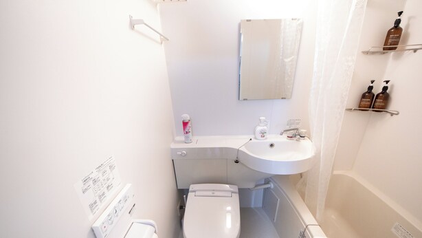 Un baño pequeño con inodoro, lavamanos y bañera. Hay artículos de aseo en la pared y un dispensador de papel.