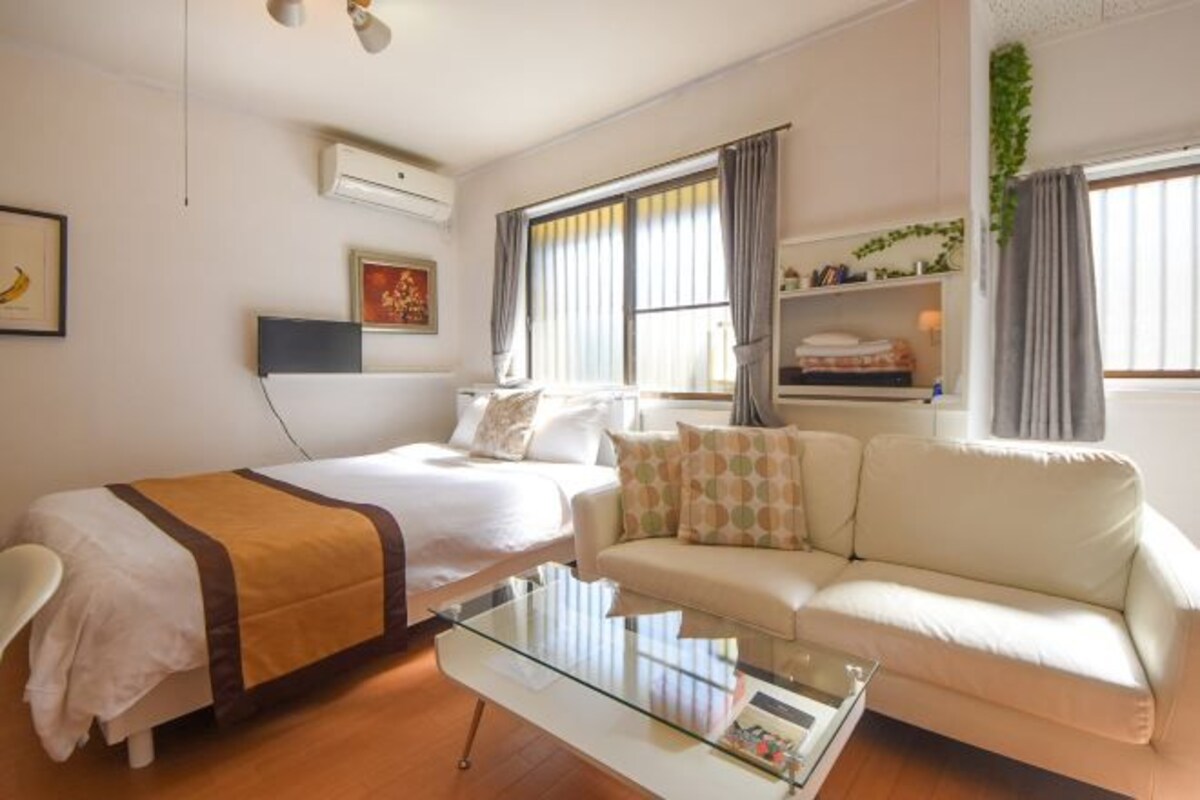 A modern hotel room with a bed, a sofa, a glass coffee table, and a window with curtains.