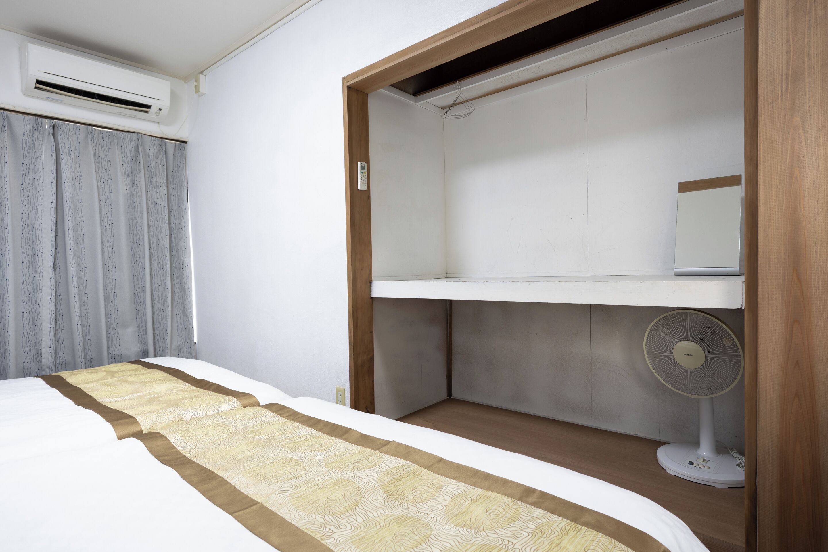 A bedroom with a bed, a bedside table, a wardrobe, and a standing fan.
