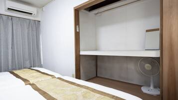 A bedroom with a bed, a bedside table, a wardrobe, and a standing fan.
