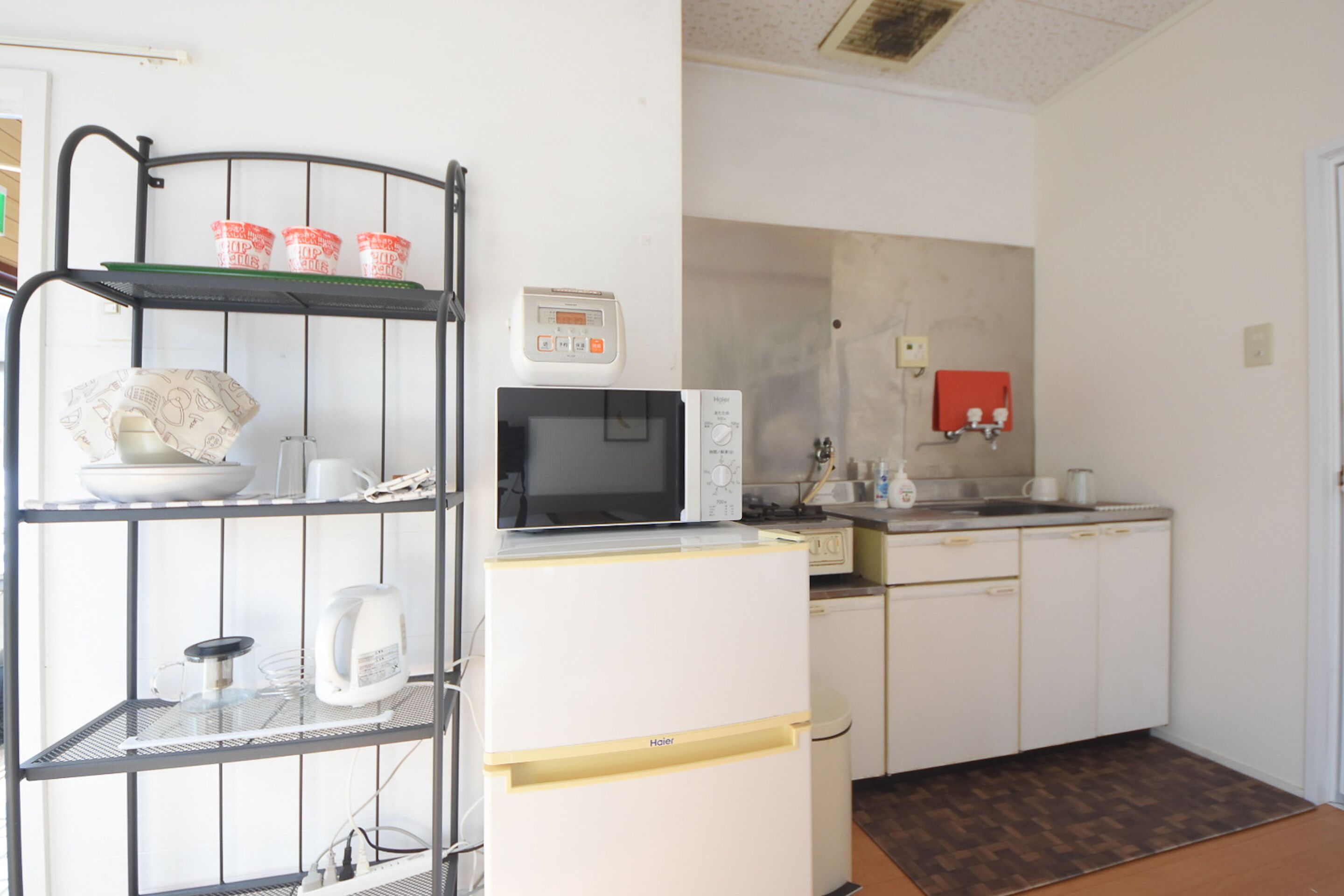 Una cocina compacta con microondas, un refrigerador pequeño y un estante metálico.