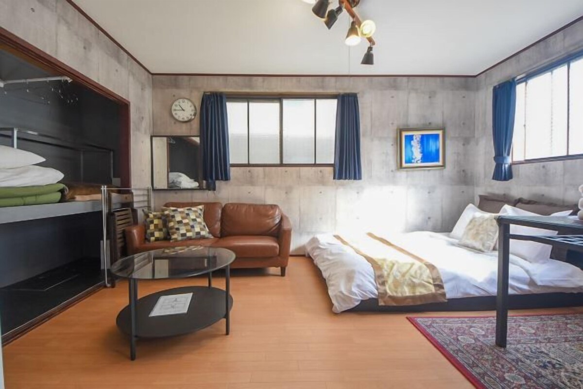 Habitación de hotel con cama, sofá, mesita de vidrio, armario y ventana con cortinas.
