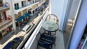 Varanda com uma pequena mesa e cadeiras, dando vista para uma rua com carros estacionados e um fileira de prédios.