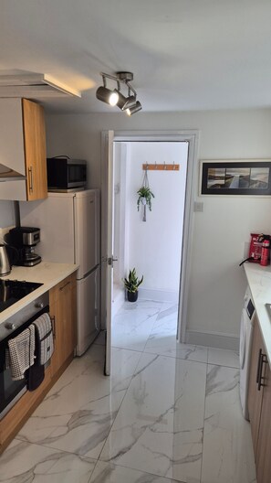 Una cocina moderna con refrigerador, microondas, cafetera y una planta colgante.