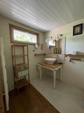 A compact bathroom with a wooden shelf, a sink, a mirror, and a window. - 🌸 L'Oasis Vacation Rental (Grazac)