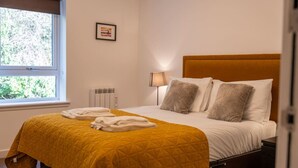 Une chambre d’hôtel avec un lit, une fenêtre, un radiateur et un tableau encadré au mur.