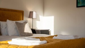 A neatly made bed with white linens and a folded towel, a bedside lamp, and a painting on the wall.