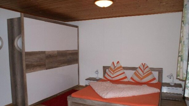 A bedroom with a wooden bed, a red rug, and a nightstand with a lamp. - Apartment Bodensdorf near Gerlitzen Ski Area (Bodensdorf am Ossiachersee)