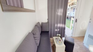 A modern living room with a grey sofa, a small white side table with a vase, and a black ottoman.