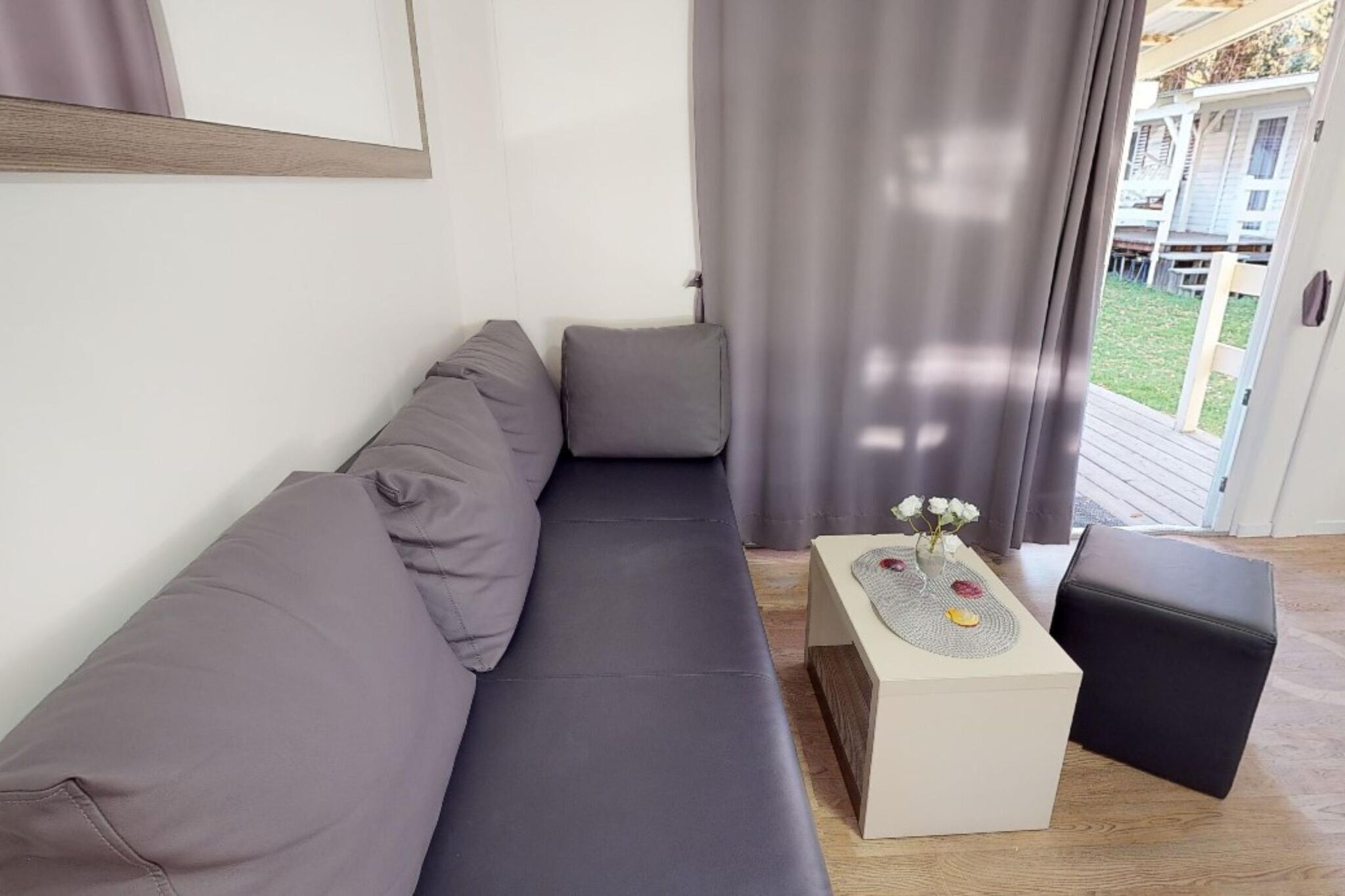 Ein modernes Wohnzimmer mit einem grauen Sofa, einem kleinen weißen Beistelltisch mit Blumen und einem schwarzen Hocker.