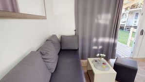Ein modernes Wohnzimmer mit einem grauen Sofa, einem kleinen weißen Beistelltisch mit Blumen und einem schwarzen Hocker.