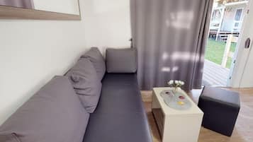 Ein modernes Wohnzimmer mit einem grauen Sofa, einem kleinen weißen Beistelltisch mit Blumen und einem schwarzen Hocker.