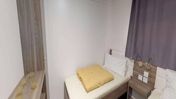 A small, neatly arranged bedroom with a single bed, a bedside table, and a nightstand.