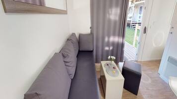 Una sala moderna con un sofá gris, una mesita auxiliar blanca con un florero y un taburete negro.
